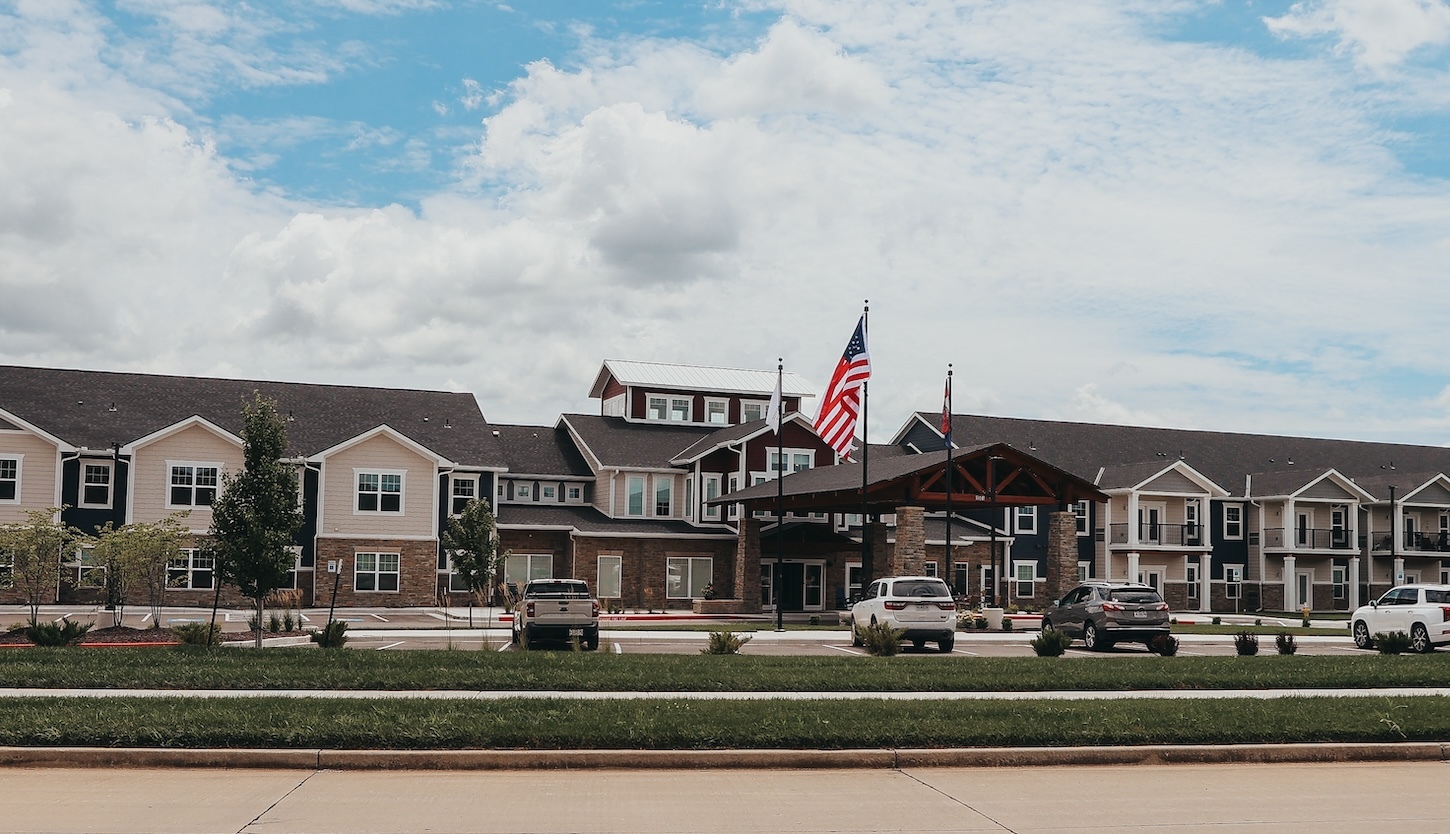 Clear Creek Village, a boutique life care community in Tiffin, Iowa, featuring modern architecture, American flags, and landscaped entrance with parking area.